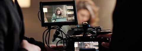 Camera rig with an attached monitor framing a woman working at a laptop on set