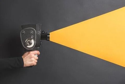 Hand holding a vintage cine camera that projects a yellow beam across a dark grey background