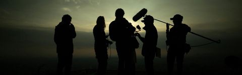 Silhouetted video crew with a camera and a boom microphone against an evening sky