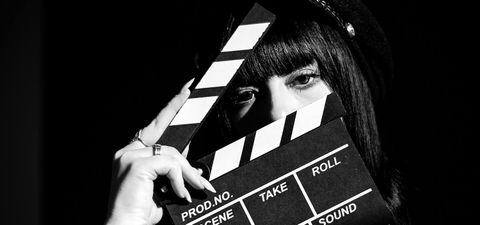 Black and white photo of a woman peering out from behind a film clapperboard