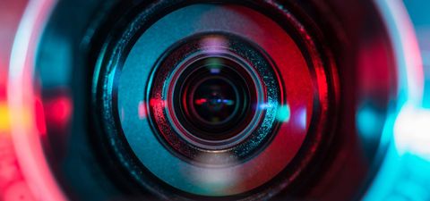 Close-up of a camera lens with red and blue light reflecting off the glass