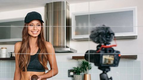Woman in a black cap standing in a kitchen on the left third of a rule of thirds grid, with a camera and microphone on a tripod in the right foreground