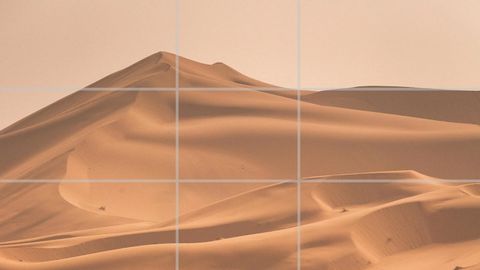 Desert sand dunes under a pale sky with a rule of thirds grid overlay, the top of the dunes sitting near the upper third line