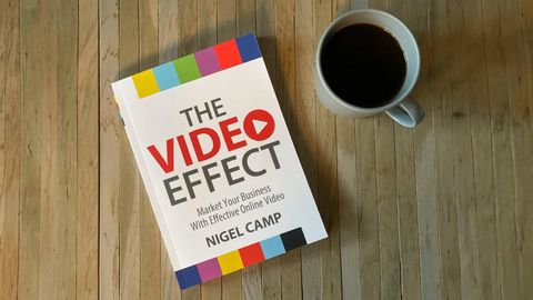The Video Effect by Nigel Camp, a paperback with colour-bar stripes on the cover, on a wooden table next to a cup of coffee