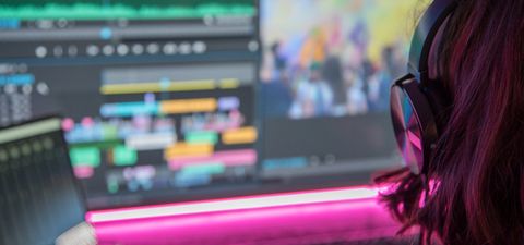 Editor in headphones looking at a colourful editing timeline on a monitor, lit by a pink light strip