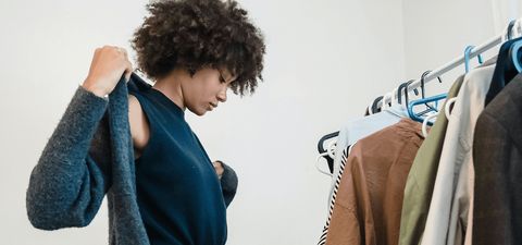 Woman putting on a grey cardigan beside a clothes rail of shirts and jackets